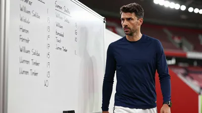 A 35-year-old, 5'11" tall, athletic-looking, male Arsenal coach or assistant coach, wearing a navy blue, long-sleeved...