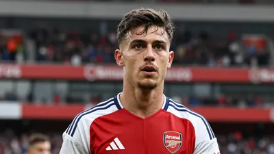 A determined 25-year-old Arsenal defender, wearing the red and navy home kit with the Arsenal crest on the chest, looks...