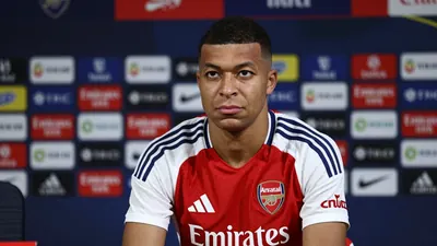A medium shot of a tall, athletic, 22-year-old Brazilian midfielder in his mid-20s, with a stern expression, sitting...