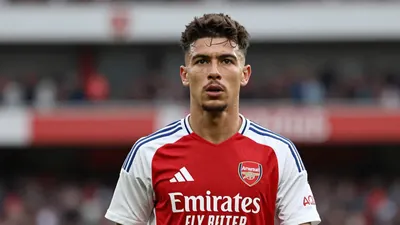 Waist-up shot of a young, athletic Arsenal player in a clean white and red jersey, focused on intense determination in...