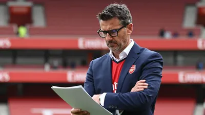 A medium shot of a mid-thirties, ruggedly-built, dark-haired, bespectacled Arsenal transfer negotiator, with a determined...