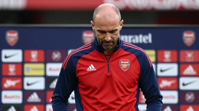 A close-up shot of a 30-year-old, 6'1" tall, athletic build, balding, dark-haired, Arsenal assistant coach, dressed in...