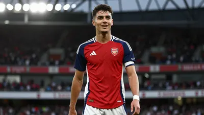 Young Arsenal academy midfielder, early 20s, athletic build, waist-up, wearing Arsenal home kit - red shirt with navy...