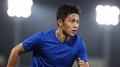 A focused, athletic 24-year-old male forward in a solid royal blue jersey, mid-stride